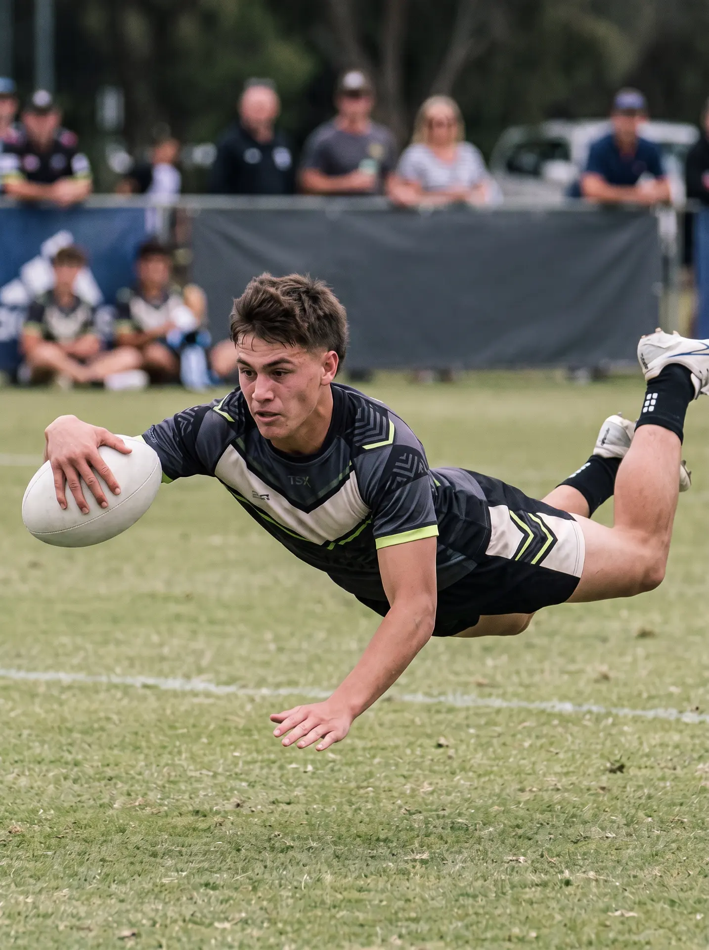 A junior rugby league player diving to ground the ball in a match.