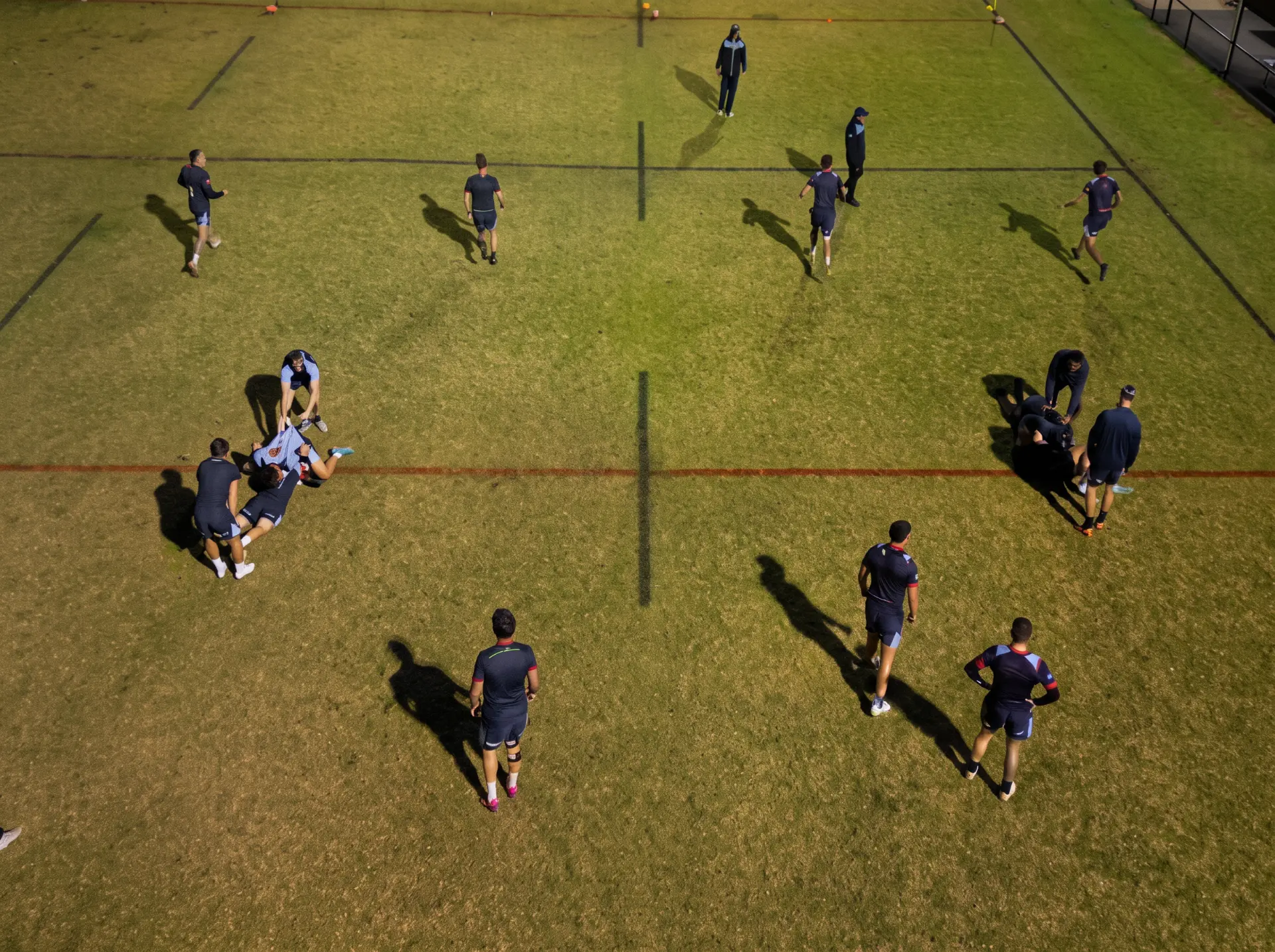 Overhead view of a training ground with several groups of players and coaches working across marked lines.
